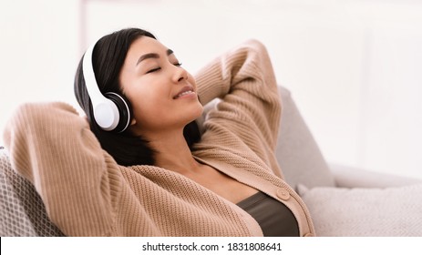 Rest And Relax Concept. Closeup Portrait Of Calm Asian Woman Lying On Couch, Listening To Music, Audio Book, Podcast, Enjoying Meditation For Sleep And Peaceful Mind In Wireless Headphones, Copy Space