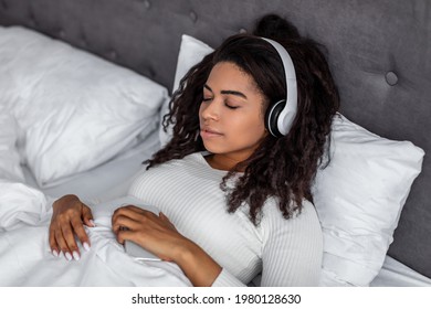 Rest And Relax Concept. Closeup Portrait Of Calm Black Woman Lying In Bed, Listening To Music, Audio Book, Podcast, Enjoying Meditation For Sleep And Peaceful Mind In Wireless Headphones. Zen-like