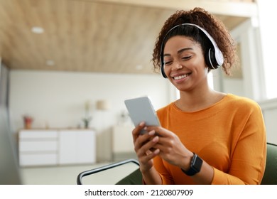 Rest And Relax Concept. Portrait of smiling African American woman using cell phone wearing wireless headset listening to music online, cheerful casual lady enjoying her playlist, free copy space - Powered by Shutterstock