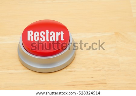A Restart red push button, A red and silver push button on a wooden desk with text  Restart
