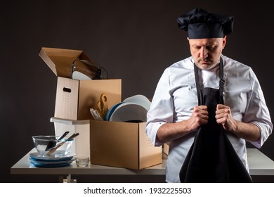 Restaurant Bankruptcy. Restaurant Industry Crisis. Closing Of The Cafe. Sad Cook Next To Packed Dishes. Ruin In The Restaurant Business. Man Has Cleared Away The Dishes And Is Taking Off Chef Uniform.