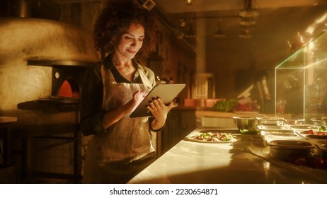 In Restaurant: Beautiful Female Chef Using Laptop Computer. Authentic Pizza Place Cooking Delicious Organic Eco Food. Bi-racial Female Entrepreneur Working on Online Order, Small Business Family Shop - Powered by Shutterstock