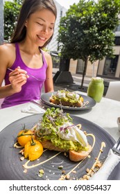 Restaurant Breakfast Brunch Avocado Toast With Eggs Woman Eating Plate At Cafe. Two Meals Couple Enjoying Morning Together On Outdoor Street Terrace.