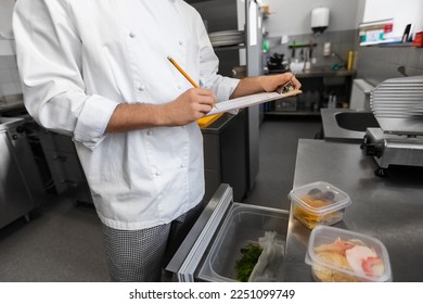 restaurant business, profession and people concept - close up of male chef with clipboard doing inventory in kitchen fridge - Powered by Shutterstock