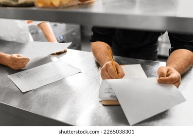 restaurant business, profession and people concept - close up of male chef with clipboard and bills filling papers on kitchen - Powered by Shutterstock