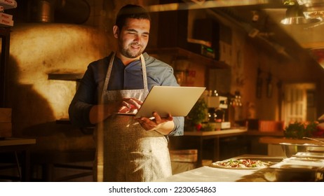 In Restaurant: Handsome Male Chef Using Laptop Computer. Authentic Pizza Place Cooking Delicious Organic Eco Food. Bi-racial male Entrepreneur Working on Online Order in Small Business Family Shop - Powered by Shutterstock