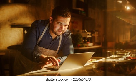 In Restaurant: Handsome Male Chef Using Laptop Computer. Authentic Pizza Place Cooking Delicious Organic Eco Food. Bi-racial Male Entrepreneur Working on Online Order in Small Business Family Shop - Powered by Shutterstock