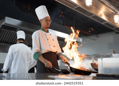 Restaurant Kitchen Action. Chef cook food with fire at kitchen restaurant Cook with wok at kitchen Chef male in uniform hold wok with fire. Сhef in the professional kitchen with a frying pan.. - Powered by Shutterstock