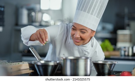 Restaurant Kitchen: Black Female Chef Fries Uses Pan, Seasons Dish with Herbs and Spices, Smiles. Professional Cooking Delicious and Traditional Authentic Food. Healthy Dishes Prepare. Medium Shot - Powered by Shutterstock