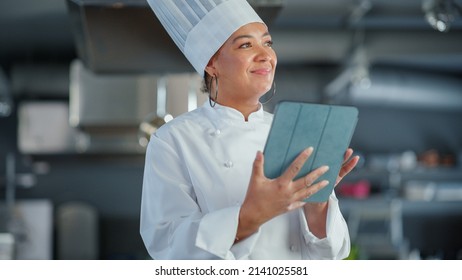 Restaurant Kitchen: Black Female Chef Cooking Delicious and Authentic Food, Uses Digital Tablet Computer. Professional Creates traditional Dish, using Healthy Ingredients for Recipe Preparation - Powered by Shutterstock