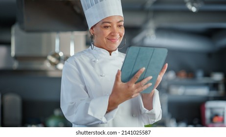 Restaurant Kitchen: Black Female Chef Cooking Delicious and Authentic Food, Uses Digital Tablet Computer. Professional Creates traditional Dish, using Healthy Ingredient, Prepare Meal Recipe. Medium - Powered by Shutterstock