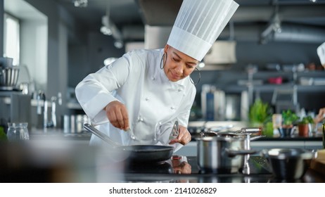 Restaurant Kitchen: Black Female Chef Fries Organic Patty on a Pan, Seasons it and Flips Cutlet with a Smile. Cooking Delicious and Traditional Authentic Food. Healthy gourmet Dishes. Medium Shot - Powered by Shutterstock