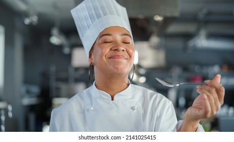 Restaurant Kitchen: Portrait of Black Female Chef Preparing Dish, Tasting Food and Enjoying it. Professional Cooking Delicious, Authentic, traditional Food, using Healthy Ingredients for Meal Recipe - Powered by Shutterstock