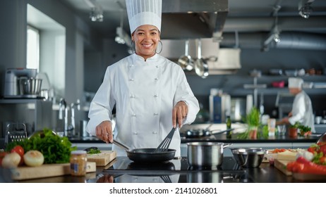 Restaurant Kitchen: Portrait of Black Female Chef in Action, Uses Pan to Cook Delicious, Traditional Authentic Food, Looks at Camera and Smiles. Healthy gourmet Dishes. Medium Wide Shot - Powered by Shutterstock