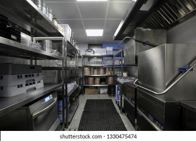 Restaurant Kitchen Storage Room With Stacks Of Plates, Glasses On Metal Shelves, Dishwashers And Rubber Honey-comb Rugs On The Floor  