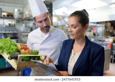 restaurant manager talking to male chef in commercial kitchen - Powered by Shutterstock