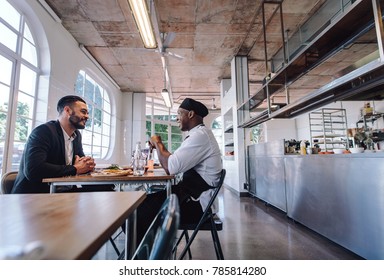 Restaurant Manager Talking With A Professional Chef. Cafe Owner And Cook Sitting At A Table And Talking.