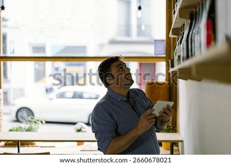 Restaurant manager using digital tablet checking stock and taking inventory of wine bottles on shelf