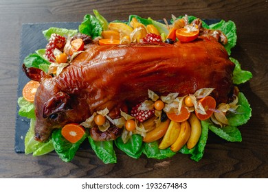 Restaurant menu. Baked suckling pig whole on a stone decorative board with fruit and physalis. Top view. - Shutterstock ID 1932674843