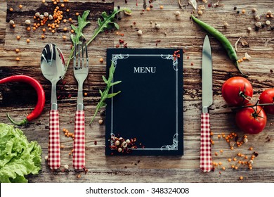 Restaurant menu. Top view of chalkboard menu laying on the rustic wooden desk with vegetables around - Shutterstock ID 348324008