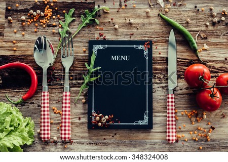 Restaurant menu. Top view of chalkboard menu laying on the rustic wooden desk with vegetables around
