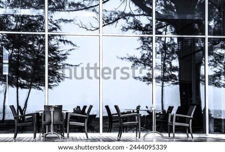 Restaurant at Nai Yang Beach, Island Phuket, Thailand. Trees and sea are reflected in glass front. 
Tables and chairs in front of glass facade. Trees and sea are reflected in glass front.