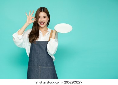 Restaurant owner sme Asian woman showing OK sign and holding empty white plate or dish isolated on green background