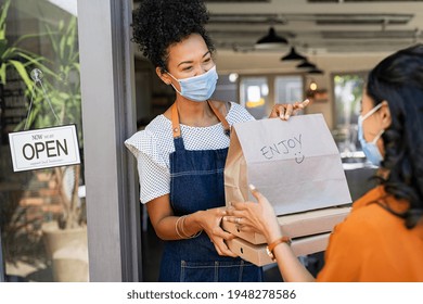 Restaurant Owner Working Only With Take Away Orders During Corona Virus Outbreak. Young Black Woman Wearing Face Mask Giving Takeout Meal To Customer Outside Her Cafeteria. Customer Pick Up Take-away.