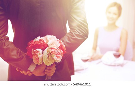 restaurant, people, celebration and holiday concept - close up of man hiding flowers behind from woman at restaurant - Powered by Shutterstock