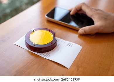 Restaurant queue pager placed on receipt on wooden table. Perfect for concepts of food service technology, customer waiting system, smart restaurant operations, and digital order notification tools.