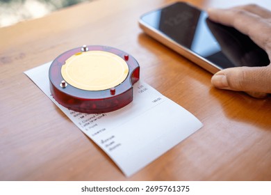 Restaurant queue pager placed on receipt on wooden table. Perfect for concepts of food service technology, customer waiting system, smart restaurant operations, and digital order notification tools.