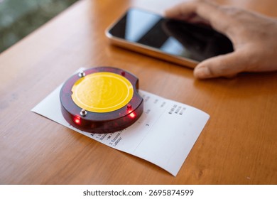 Restaurant queue pager placed on receipt on wooden table. Perfect for concepts of food service technology, customer waiting system, smart restaurant operations, and digital order notification tools.
