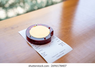 Restaurant queue pager placed on receipt on wooden table. Perfect for concepts of food service technology, customer waiting system, smart restaurant operations, and digital order notification tools.