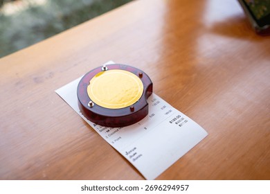 Restaurant queue pager placed on receipt on wooden table. Perfect for concepts of food service technology, customer waiting system, smart restaurant operations, and digital order notification tools.