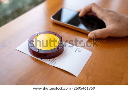 Restaurant queue pager placed on receipt on wooden table. Perfect for concepts of food service technology, customer waiting system, smart restaurant operations, and digital order notification tools.