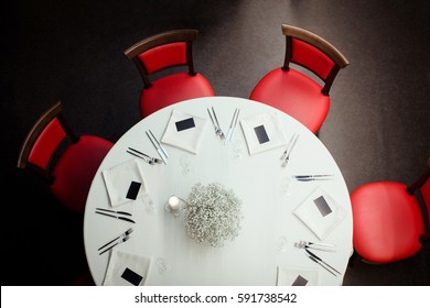 Restaurant Round Table Covered With A White Tablecloth And Served And Red Chairs Around It. From Above. 