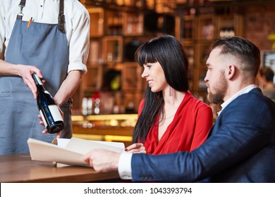 Restaurant service. young couple and waiter offerring bottle of a wine - Powered by Shutterstock