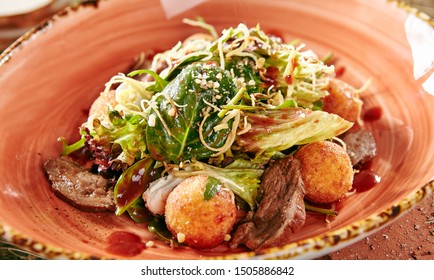 Restaurant Starter Menu Of Duck Breast Salad With Crispy Potato Balls On Rustic Style Hay Background Close Up. Macro Photo Of Meat Salat With Whole Potatoes, Soft Cheese, Lettuce And Arugula Leaves