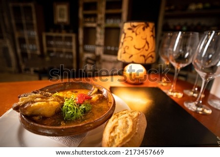 restaurant table with Bolivian fricassee plate with a closed menu, glasses, a small lamp with warm light and a cabinet with bottles and glasses in the background