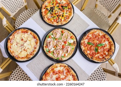 Restaurant table with five delicious assorted pizzas including pepperoni, vegetable, seafood and more. Irresistible aroma of freshly baked pizza.