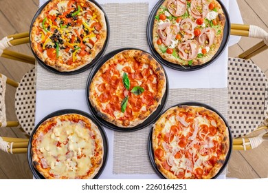 Restaurant table with five delicious assorted pizzas including pepperoni, vegetable, seafood and more. Irresistible aroma of freshly baked pizza.