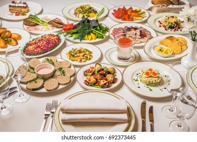 Restaurant Table, Many Different Dishes. Plates, Forks, Knives, Glasses On A White Tablecloth. Delicious Healthy Fresh Food.