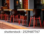 A restaurant veranda with black wooden chairs on red legs. Summer cafe with plants and red brick wall in the background.