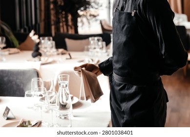 Restaurant waiter arranging table setting before service in fine dining interior, hospitality and customer experience concept.