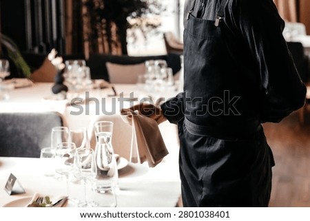Restaurant waiter arranging table setting before service in fine dining interior, hospitality and customer experience concept.