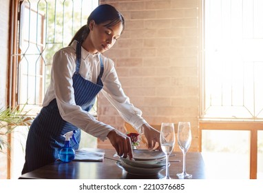Restaurant waitress cleaning dishes from table after a meal. Customer service, diner and working in the food industry as a waiter clearing dirty plates, glasses and leftovers to clean dinner table