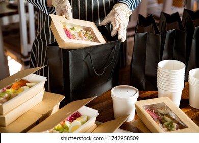 Küchenarbeitnehmer mit Schutzmaske und Handschuhen, die Lebensmittel verpacken, nehmen Sie weg. Lebensmittelzustellungsdienste und Online-Einkäufe für kontaktlose Lebensmittel.
