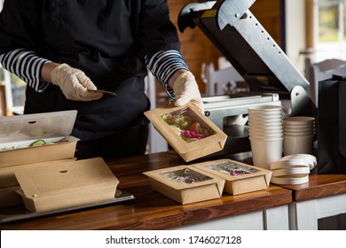 Restaurant worker wearing protective mask and gloves packing food boxed take away. Food delivery services and Online contactless food shopping.
				