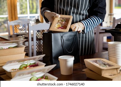 Restaurant Worker Wearing Protective Mask And Gloves Packing Food Boxed Take Away. Food Delivery Services And Online Contactless Food Shopping.
