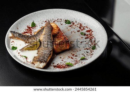 restaurant-style presentation of Seabass with potato gratin and celery sauce, elegantly served on a black table. Perfect choice for culinary promotions and food enthusiasts